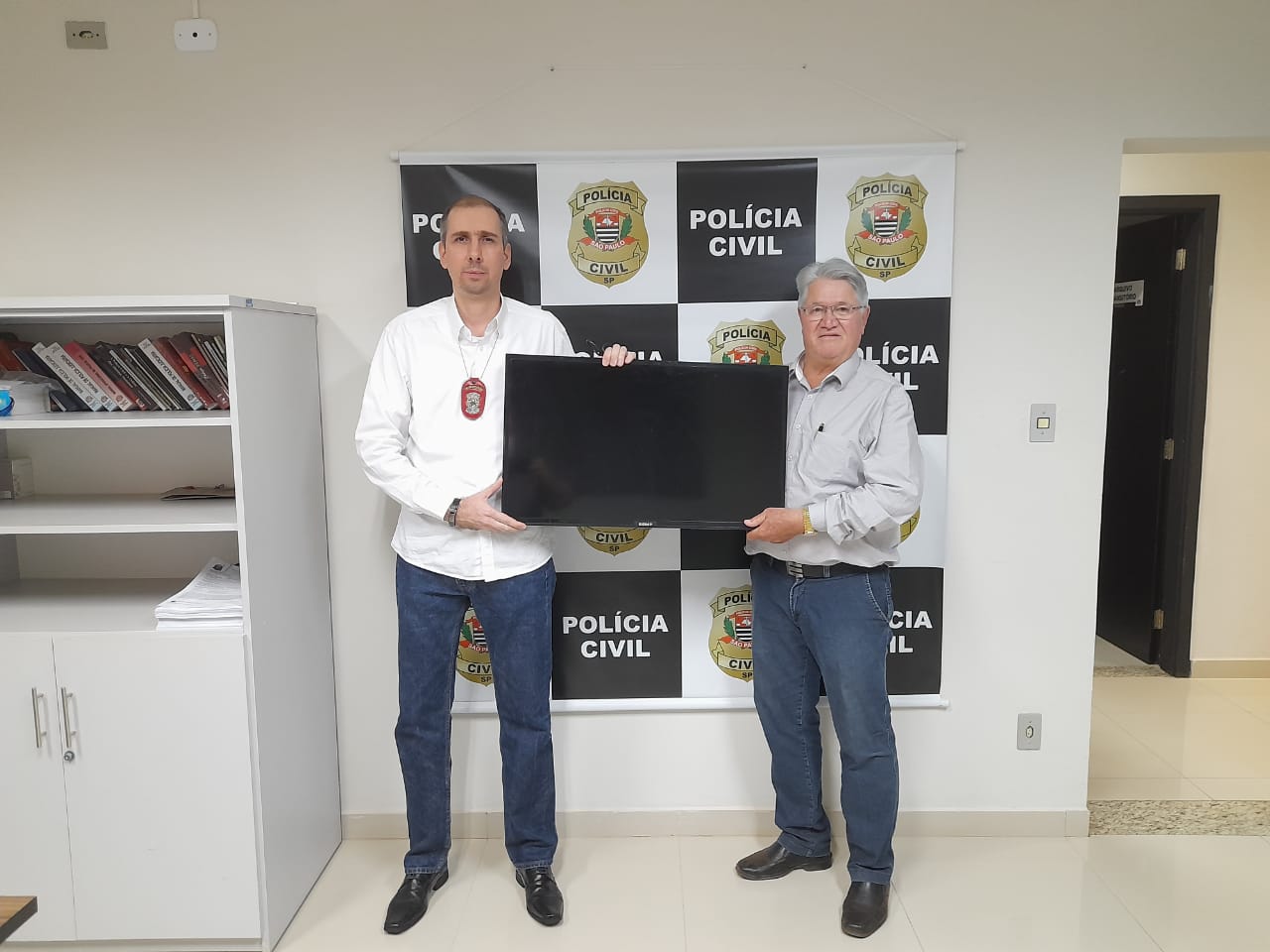 Prefeito Bica recebe televisão das mãos do delegado de polícia, Dr. Sérgio Augusto Ugatti Durão. Foto: divulgação.