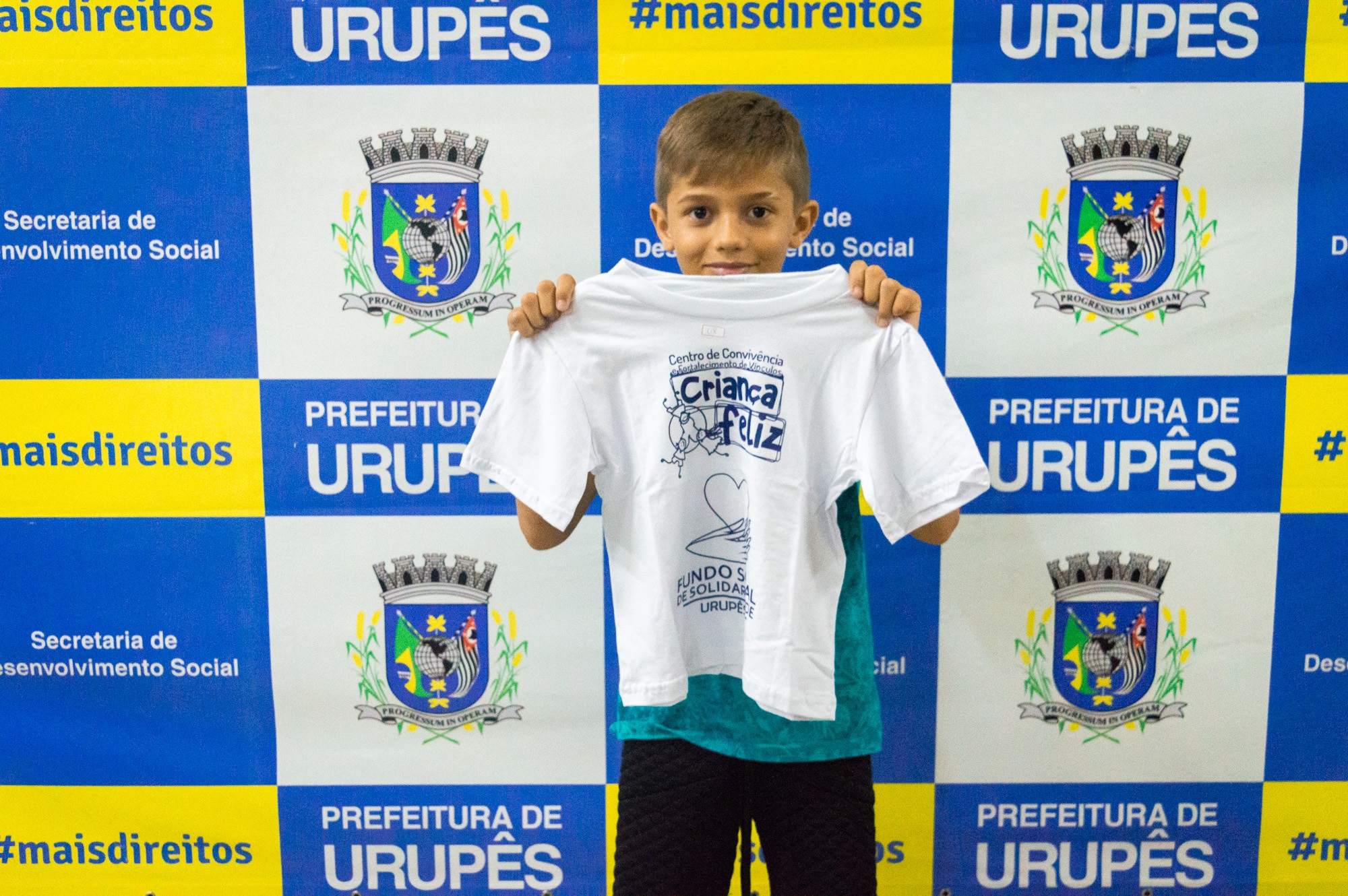Aluno mostra camiseta do camiseta durante a cerimônia de entrega dos uniformes dos alunos do projeto Criança Feliz. Foto: Carina Costa / Prefeitura Municipal de Urupês.